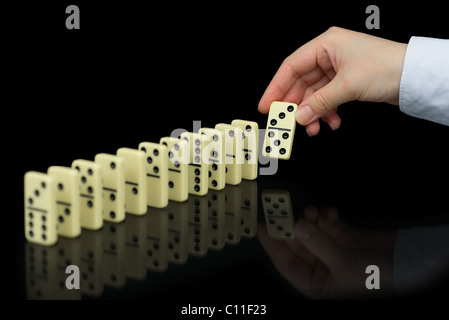 Mano costruisce una linea di domino su sfondo nero Foto Stock