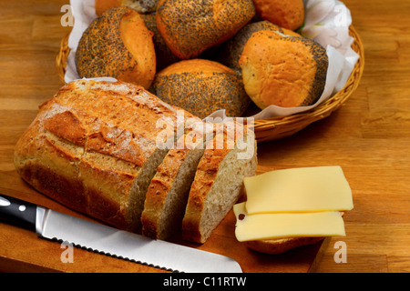 Pane fresco formaggio e il coltello sul tagliere di legno con cesto con pane in background Foto Stock