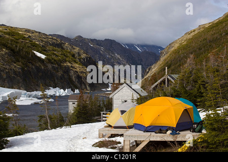 Storico Campo Felice, tenda sulla piattaforma di legno, la molla lo sgretolamento, fusione, neve creek dietro, Chilkoot Trail, Chilkoot Pass Foto Stock