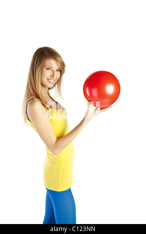 Felice giovane donna bionda in piedi in punta di piedi e tenendo palla rossa Foto Stock