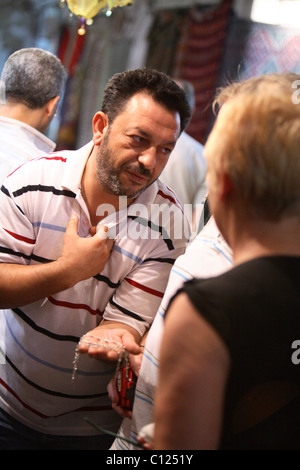 Commerciante cercando di vendere gioielli al passaggio di turisti. Mercato Souk Tunisi Tunisia Africa usando gesti espressivi Foto Stock