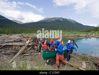 Gli uomini portaging, portando una canoa sulla terraferma aggirando ostacolo, log jam dietro, superiore Liard River, Yukon Territory, Kanada Foto Stock