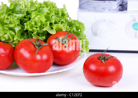 Pomodori, insalata verde foglia e processore da cucina sul tavolo bianco Foto Stock