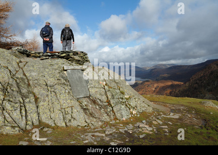 La Lapide ai Caduti di Borrowdale sulla sommità della rupe del castello con due escursionisti tenendo nella vista Foto Stock