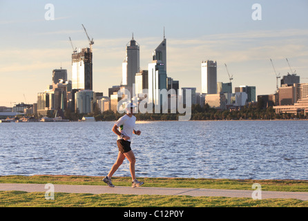 Uomo di jogging sul percorso accanto al fiume con la città sullo sfondo. Foto Stock