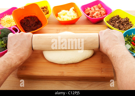 Preparazione pizza; le mani con il mattarello sulla pasta e gli ingredienti in primo piano Foto Stock