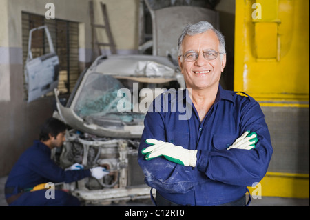 Ritratto di un meccanico automatico sorridente con un apprendista di riparazione di un auto in background Foto Stock