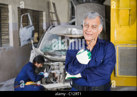 Ritratto di un meccanico automatico sorridente con un apprendista di riparazione di un auto in background Foto Stock