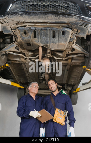 Auto meccanico con un apprendista in piedi sotto un rilievo auto in un garage Foto Stock