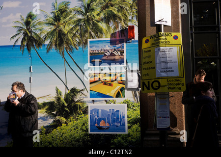 L'uomo mangia sandwich con costruzione sito che mostra tropical beach paradise e immagini di città del mondo con un parcheggio non firmare. Foto Stock