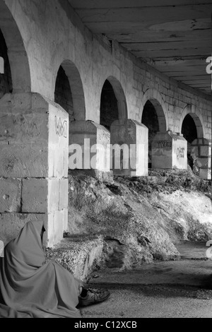 Una persona senza dimora seduto sul pavimento in un inquietante sottopassaggio a freddo. Foto Stock