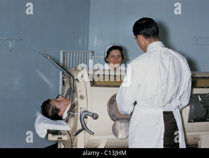 Il personale ospedaliero sono l' esame di un paziente in un serbatoio respiratore, polmone di ferro, durante una Rhode Island epidemia di polio. Il polmone di ferro racchiusi la cavità toracica esternamente in una camera a tenuta d'aria. La camera è stata utilizzata per creare una pressione negativa intorno alla cavità toracica, facendo così in modo che l'aria a rush nei polmoni per equalizzare la pressione intrapolmonare. Ca. 1960. Foto Stock