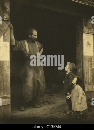 Un cuoio aproned fabbro nella porta della sua fucina di parlare per due ragazzi. Fotografia di Francesca Stebbins Allen, c. 1900. Foto Stock