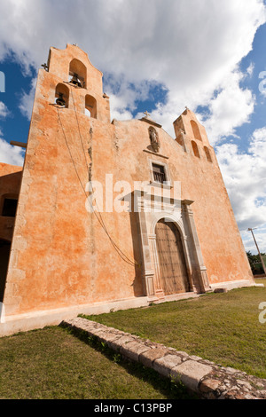 Facciata anteriore angolata della chiesa francescana di Mani. Adobe ocra, una massiccia porta di legno e uno di lavoro campanile domina Foto Stock