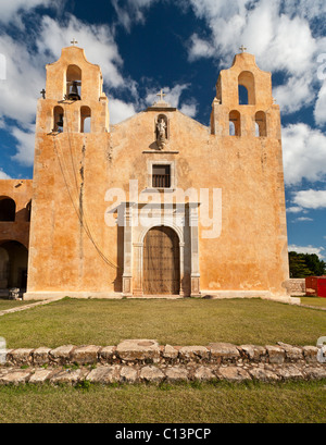 Facciata anteriore a della chiesa francescana in mani verticale. Adobe ocra, una massiccia porta di legno e uno di lavoro campanile domina Foto Stock