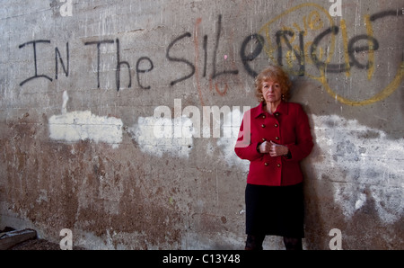 Questo leggermente inquietante immagine stock come graffiti dicendo "nel silenzio" su un muro di cemento con una matura più vecchi donna caucasica. Foto Stock