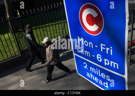 Due pedoni camminare sotto un degli automobilisti Zona di Congestione segno su una strada di Londra. Foto Stock