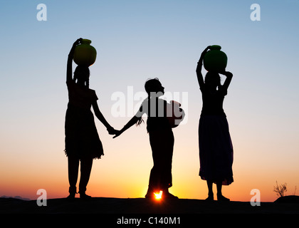 Rurale villaggio indiano ragazze con vasi d'acqua al tramonto. Silhouette. Andhra Pradesh, India Foto Stock