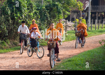 Un gruppo di giovani monaci buddisti e gli altri ragazzi sono equitazione biciclette a scuola su una strada sterrata in Laos comunista. Foto Stock