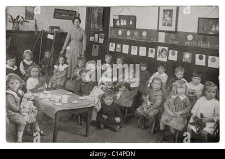 Cartolina originale dell'era WW1 dei bambini della scuola materna e infantile in classe con il loro insegnante, avendo uno spuntino, o giocando con i teacup giocattolo, circa 1913, 1914 1915 U.K. Foto Stock