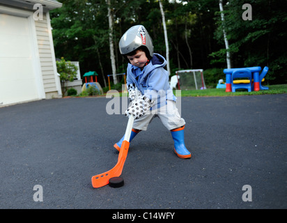 2 anno vecchio ragazzo gioca street hockey con presina guanti e stivali di gomma Foto Stock