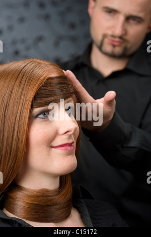 Parrucchiere professionale con lunghi capelli rossi moda modello nero al salone di lusso Foto Stock