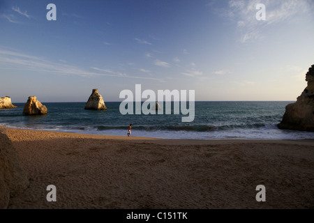 Un uomo nel nuoto shorts esegue o fa avanzare lungo una spiaggia deserta al tramonto visto da Canico ristorante di pesce in Alvor, Portogallo Foto Stock