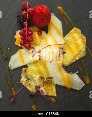 Carpaccio di [melone Honeydew] e fresche pineaple spruzzata con un coulis di mango vestito con i frutti di bosco su ardesia 116344b Food02 Foto Stock