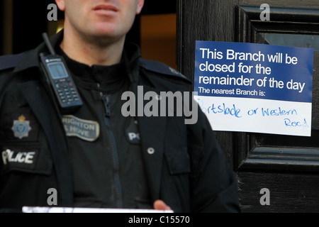 A Brighton e Hove funzionario di polizia sta di guardia al di fuori di un Natwest Bank a Hove, East Sussex, Regno Unito. Foto Stock