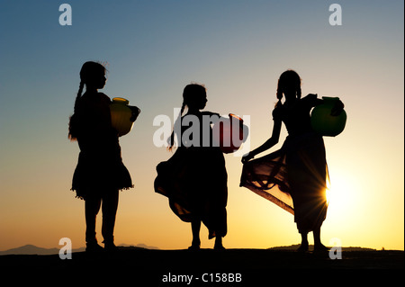 Rurale villaggio indiano ragazze con vasi d'acqua al tramonto. Silhouette. Andhra Pradesh, India Foto Stock