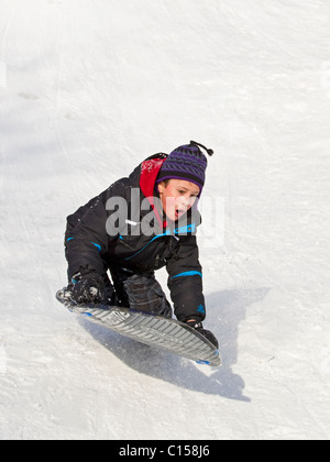 Ragazzo giovane slittino giù collina innevati in inverno Foto Stock