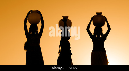 Rurale villaggio indiano ragazze il bilanciamento di una pentola di acqua sulle loro teste al tramonto. Silhouette. Andhra Pradesh, India Foto Stock