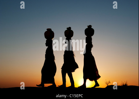 Rurale villaggio indiano le ragazze a piedi, bilanciamento vasi d'acqua sulle loro teste al tramonto. Silhouette. Andhra Pradesh, India Foto Stock