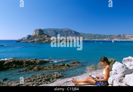 Donna che legge un libro sulla spiaggia di Nisi Kastri con Agios Stefanos sul retro, Kos Dodecaneso isole, Grecia, Europa Foto Stock