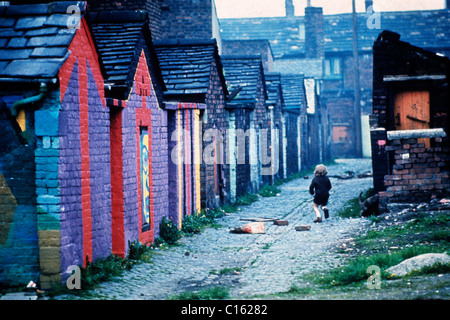 Un bambino bambino bambino che guarda dietro dietro, che gioca correndo lungo un vicolo con pitture murali colorate nel vicolo posteriore del Lancashire, Inghilterra settentrionale, anni '1970, Regno Unito, 1975, KATHY DEWITT Foto Stock