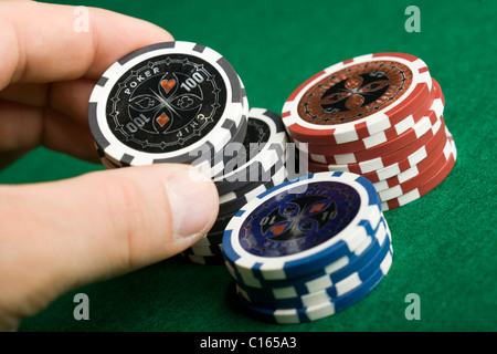 La mano di raggiungere per il nero poker chips da pile di gettoni sul feltro verde Foto Stock