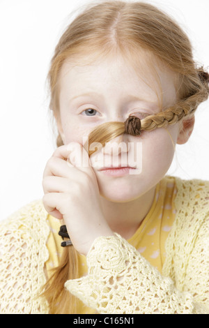 Ragazza 8 anni, tenendo una treccia di fronte ad uno dei suoi occhi Foto Stock