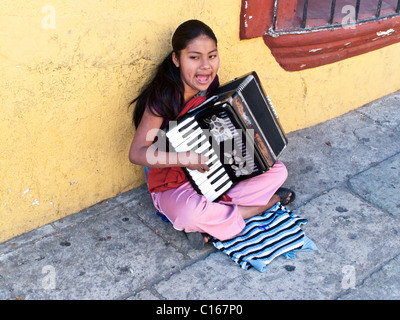 Indigeni messicani teen teenage ragazza seduta sul marciapiede contro la bellissima parete gialla a suonare la fisarmonica e canto Messico Oaxaca Foto Stock