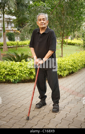 Indiano vecchio uomo asiatico sorge in un parco con un bastone da passeggio Foto Stock