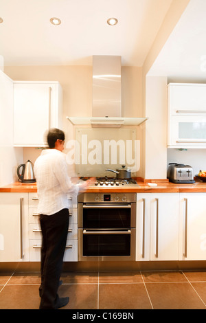 Indian donna asiatica in un elegante e moderna cucina con unità di bianco ed un piano di lavoro in legno Foto Stock