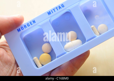 Una mano che tiene i medicamenti in una pillola organizzatore Foto Stock