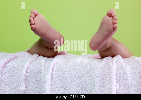 Coppia di piedi del bambino penzolante sul tovagliolo rosa contro lo sfondo di colore verde Foto Stock