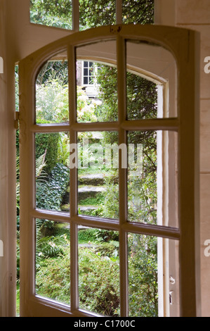 Vista attraverso il vetro aperto porta vetrata a incolto giardino Foto Stock
