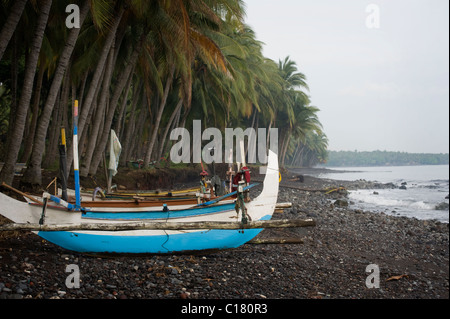 Un Balinese tradizionale barca da pesca o jukung, viene trasportata fino sulla spiaggia nel villaggio di Tembok, Bali, Indonesia. Foto Stock