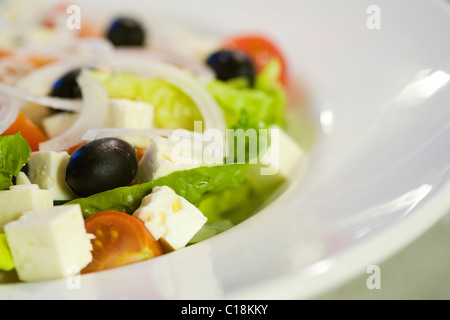 Insalata greca con pecora, Formaggio feta formaggio, pomodori, cipolle, lattuga e olive nere servita su una piastra bianca Foto Stock