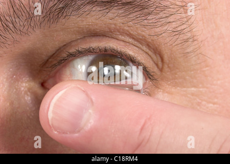 Primo piano di un uomo occhio marrone mentre inserendo un correttivo lente a contatto su un dito. Foto Stock