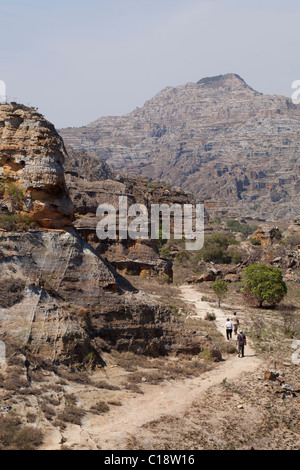 I turisti del trekking attraverso Isalo National Park, Madagascar, contro uno sfondo di Jurassic arenaria erose scogliere. Foto Stock