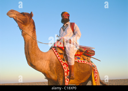 Signor deserto in tradizionale Rajput, Rajasthani che porta una spada a dorso di un cammello sulle dune di sabbia vicino a Jaisalmer, Rajasthan, India Foto Stock