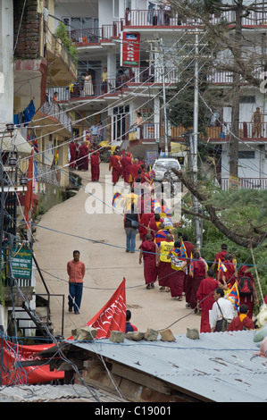 Una linea di flusso di monaci fino alla cima di una collina azienda bandiere tibetano Foto Stock