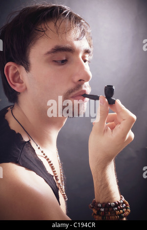 Giovane uomo di fumare poco tubo su sfondo nero Foto Stock